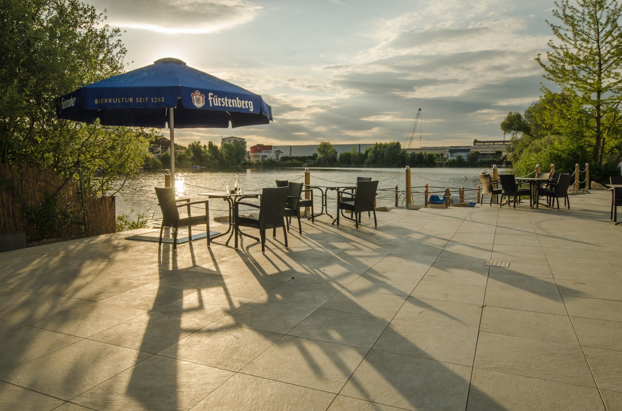 Seeterrasse mit Tischen, Stühlen und Sonnenschirm am Wasser